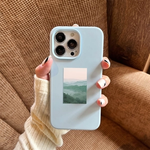 Close-up of light blue matte phone case featuring mist mountain forest illustration