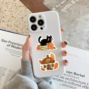 Vista detallada de pegatinas otoñales en funda blanca de móvil con motivos de libros y gatos