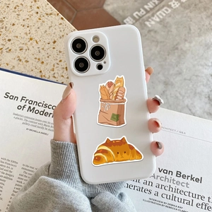 White phone case with cute cartoon cat bread stickers held against an open art book