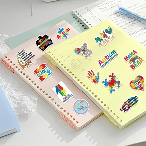 Set de 50 pegatinas de Autism Awareness para portátiles y maletas sobre un cuaderno