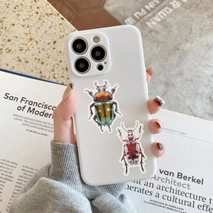 Close-up of white iPhone case with glossy metallic beetle prints on a designer desk
