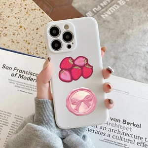 Dettaglio degli adesivi con fragole e fiocco rosa su una custodia bianca per telefono