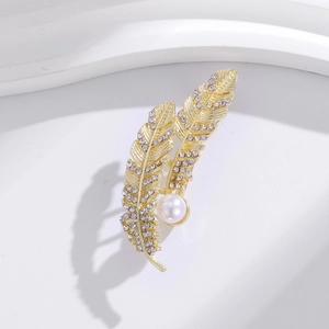 Dettaglio di elegante spilla a piuma dorata con strass scintillanti e perla bianca