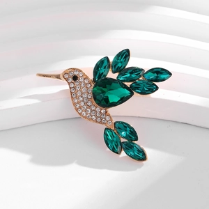 Détail de la broche colibri dorée avec cristaux émeraude et strass blancs scintillants