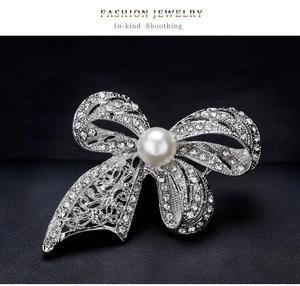 Detail view of bow brooch featuring sparkling crystals and a white round pearl center