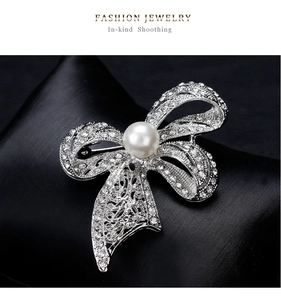 Detail shot of a silver bow brooch featuring sparkling crystals and a white center pearl