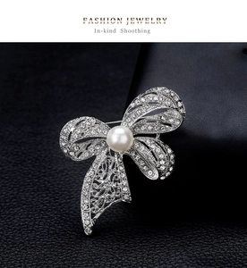 Detailed view of crystal bow brooch with a large white pearl on black leather background