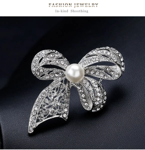 Macro shot of silver bow brooch featuring sparkling crystals and a white center pearl