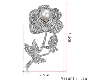 Dettaglio della spilla a rosa argentata con perla bianca e strass scintillanti