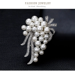 Macro shot of white pearl grape brooch with crystal leaves on black leather surface