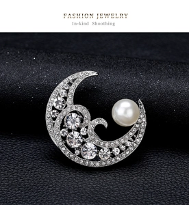 Detailed view of silver moon brooch with pavé rhinestones and a white pearl accent