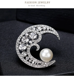 Close-up of silver moon brooch with pavé crystals and a large white round pearl