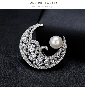 Detailed macro view of a silver crescent moon brooch with white pearls and sparkling crystals