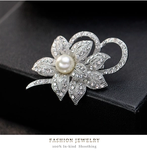 Detail of silver flower brooch featuring white rhinestones and a central round pearl