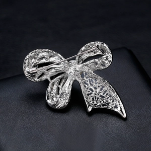 Silver bow brooch with white pearl back view showing secure safety pin on black leather