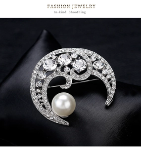 Macro detail of crescent moon brooch with shimmering crystals and large white pearl