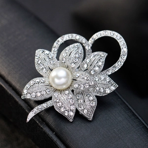 Elegant silver flower brooch with large pearl and shimmering rhinestones on a black box
