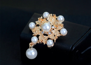 Vista macro de un broche de flor dorado con perlas blancas y colgante de cristal