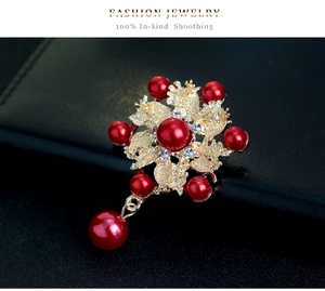 Detalle del broche de flor con perlas rojas pétalos dorados y colgante de circonita