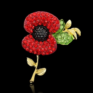 Detailed view of red rhinestone poppy brooch with green leaves on gold plating