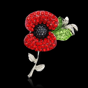 Macro detail of red rhinestone poppy brooch with silver plating and green crystals