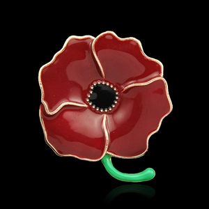 Macro detail of red enamel poppy brooch with golden edges and green stem on black background