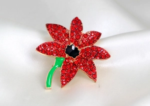 Macro shot of red rhinestone poppy brooch with gold plating on cream silk fabric