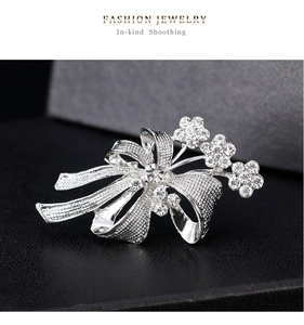 Détail d'une broche nœud argentée avec fleurs ajourées et strass brillants incrustés