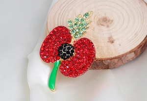 Close-up of poppy flower brooch with red rhinestones and green enamel on wood