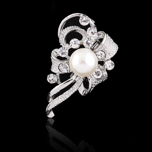 Sparkling silver bow brooch with a large white pearl and rhinestones on black background