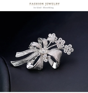 Détail de la broche nœud argentée avec fleurs ciselées et strass blancs scintillants