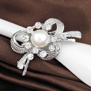 Broche nœud argentée élégante avec perle blanche et cristaux sur fond de soie marron foncé