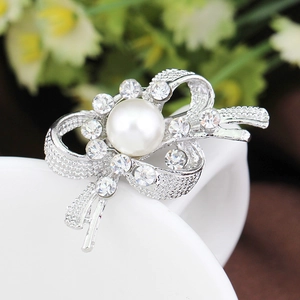 Vue rapprochée d'une broche nœud argentée ornée de cristaux et d'une perle blanche centrale