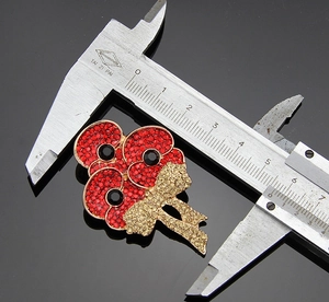Detailed view of red rhinestone poppy brooch with gold bow being measured by a caliper