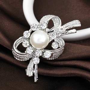 Élégante broche nœud argentée avec perle et strass brillants sur fond de soie marron foncé