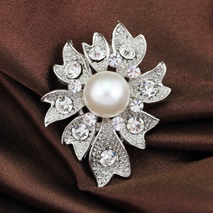 Gros plan d'une broche florale avec une grande perle blanche et pétales en cristal