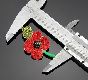 Detailed size measurement of a red poppy brooch with crystals using a caliper tool