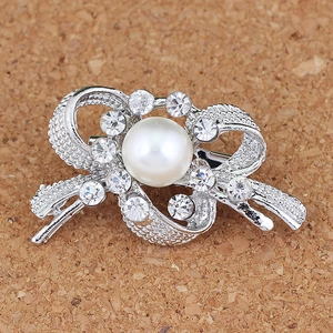 Détail d'une broche en forme de nœud avec une grande perle et des strass étincelants