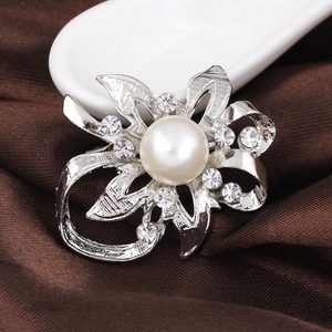 Macro detail of silver floral brooch featuring a large center pearl and crystal accents