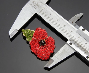 Poppy flower brooch with red rhinestones measured by caliper against black background