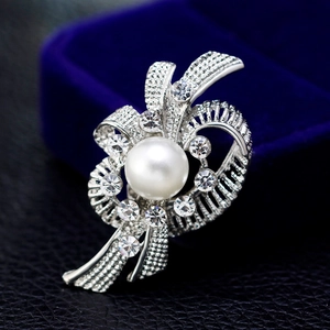Elegante silberne Schleifenbrosche mit Perle und Strass auf blauem Samtgehäuse