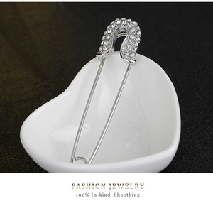 Detail shot of silver safety pin brooch with rhinestones in a white ceramic dish