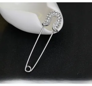 Close-up of a silver safety pin brooch with sparkling crystals on white and black base