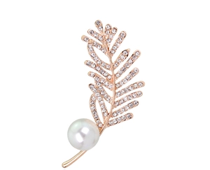 Détail macro d'une broche feuille en or rose avec strass blancs et une grande perle