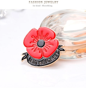 Detail of red enamel poppy brooch with black ribbon and Lest We Forget text