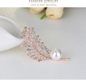 Détail de la broche plume avec strass pavés et une grande perle blanche élégante