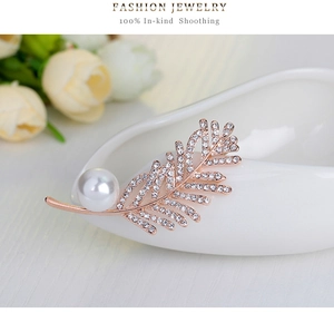 Détail de la broche en forme de feuille or rose avec strass blancs et une perle