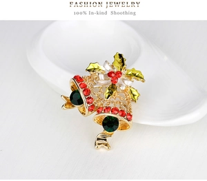 Detailed close-up of golden Christmas bell brooch with red and green rhinestones