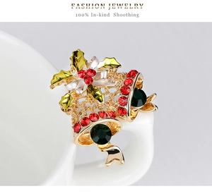 Close-up of golden Christmas bell brooch with red rhinestones and green gems on white cup