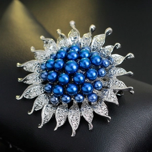 Silver sunflower brooch with deep blue pearls on a black leather background
